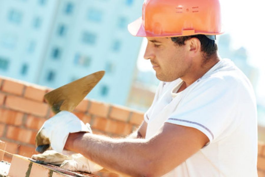construction worker. mason bricklayer installing red brick with trowel putty knife outdoors