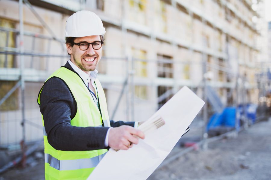 Portrait of man engineer at building site. Male construction manager wearing white helmet and yellow safety vest