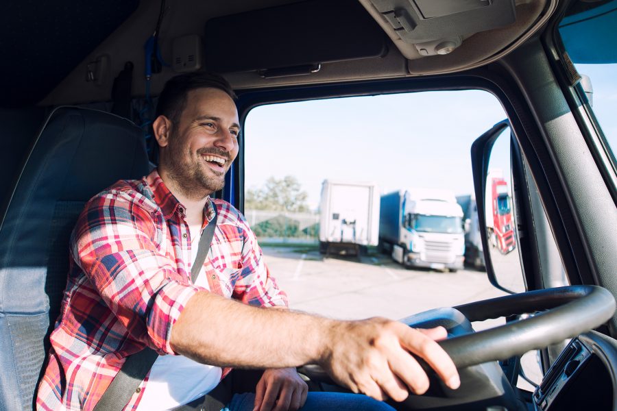 Professional middle aged truck driver in casual clothes driving truck vehicle and delivering cargo to destination.